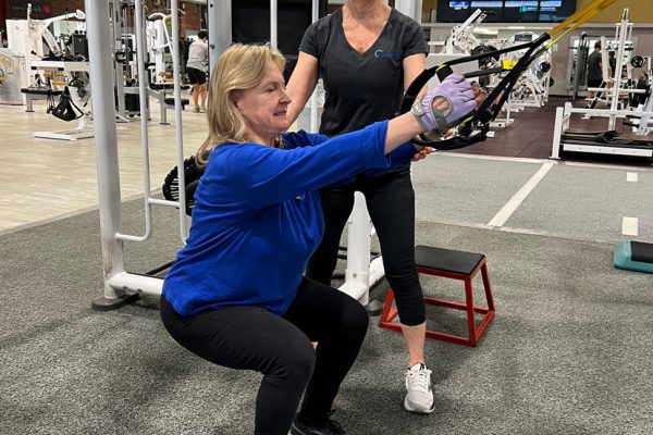 Personal trainer assists client with hands on workout in the gym.
